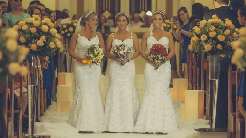 the triplet sisters walking down the aisle in similar wedding dresses, makeup, and hairstyles
